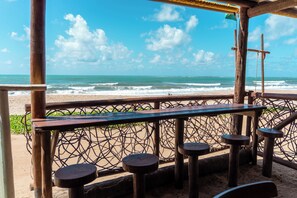 A beachside bar with a view of the ocean, wooden furniture, and a thatched roof. - Pousada La Bella Luna (Ipojuca)