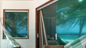 A room with a hammock, a wooden chair, and a view of palm trees through a window. - Pousada La Bella Luna (Ipojuca)