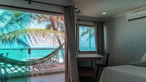 A room with a bed, a desk, and a view of the ocean with palm trees. - Pousada La Bella Luna (Ipojuca)