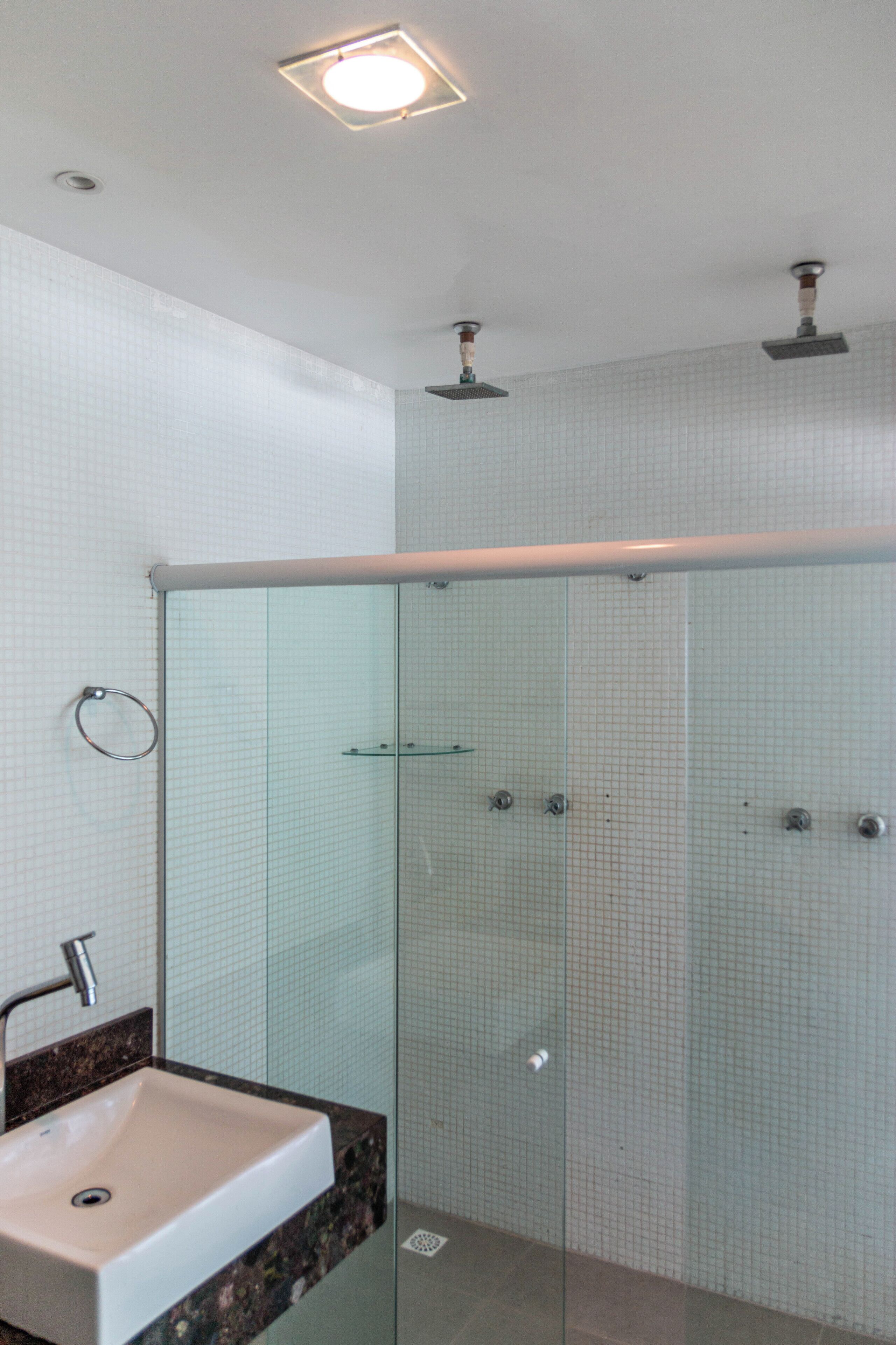 Un baño moderno con cabina de ducha de vidrio, lavamanos con encimera de mármol y lámpara en el techo.