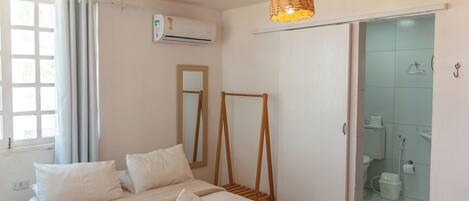 A bedroom with a bed, a mirror, a hanging light fixture, and a bathroom visible through an open door.