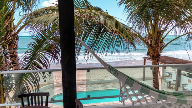 A balcony with a hammock, a pool, and a view of the ocean. - Pousada La Bella Luna (Ipojuca)