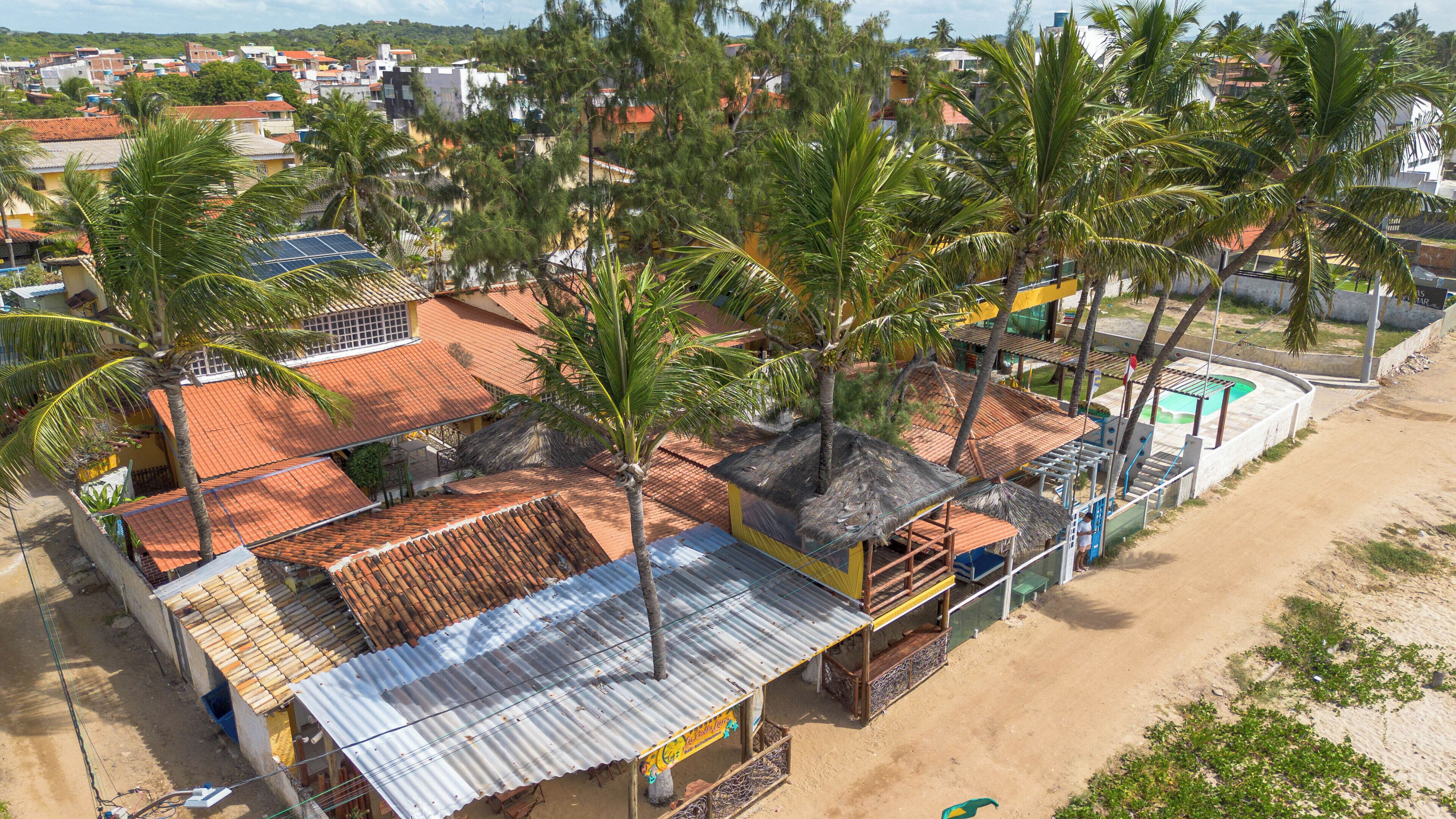 A coastal building with multiple roofs, surrounded by palm trees and a sandy beach.