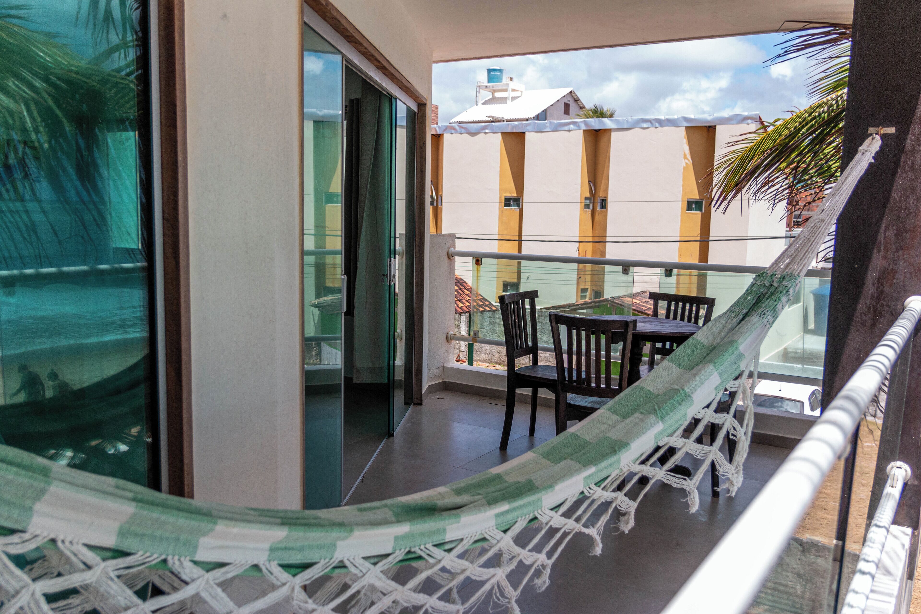 Un balcon avec un hamac, une table, des chaises et une vue sur un immeuble doté d’un réservoir d’eau.