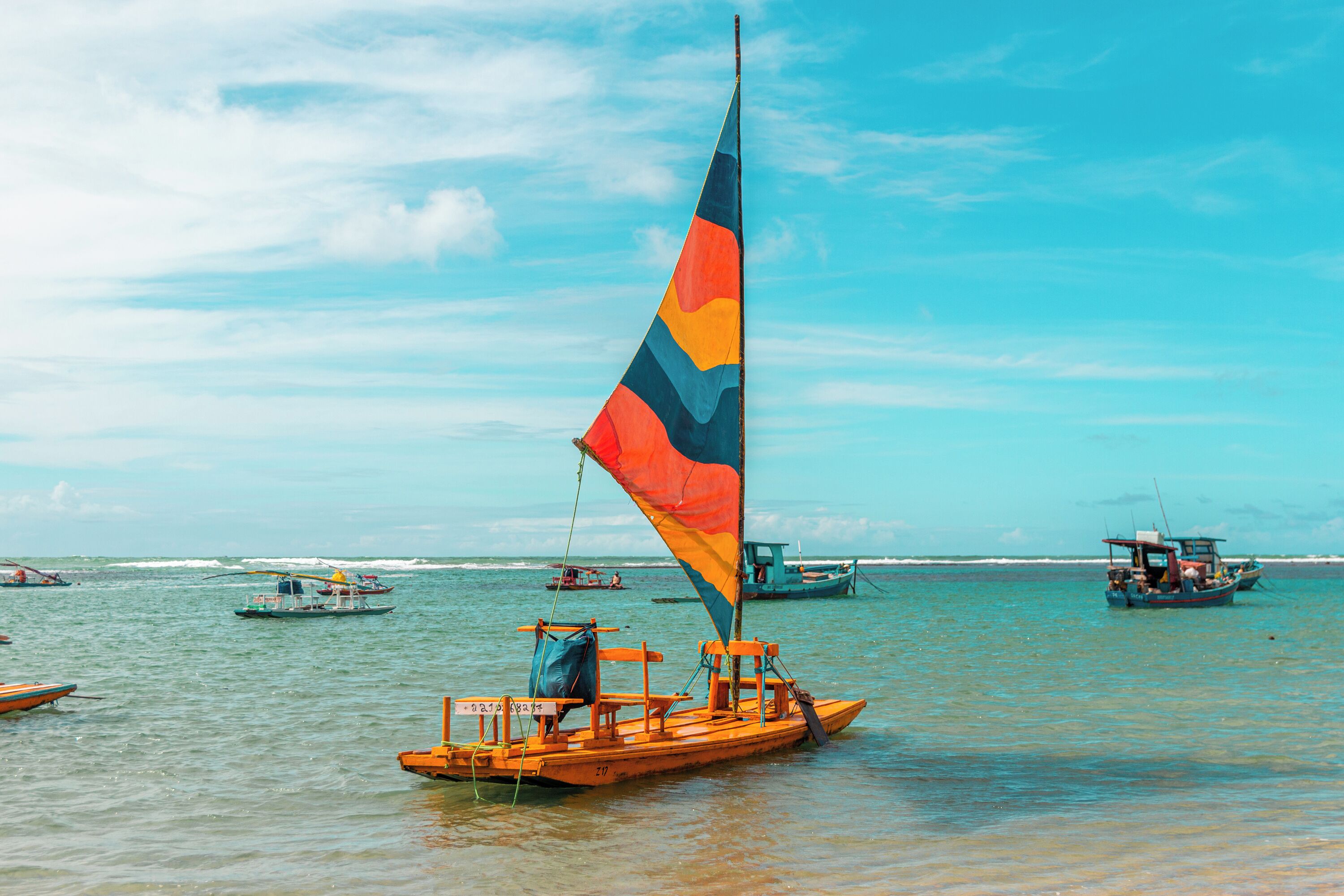 A traditional wooden boat with a colorful sail on calm waters.