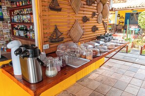 A bar area with a wooden counter, various kitchen appliances, and a shelf with bottles.