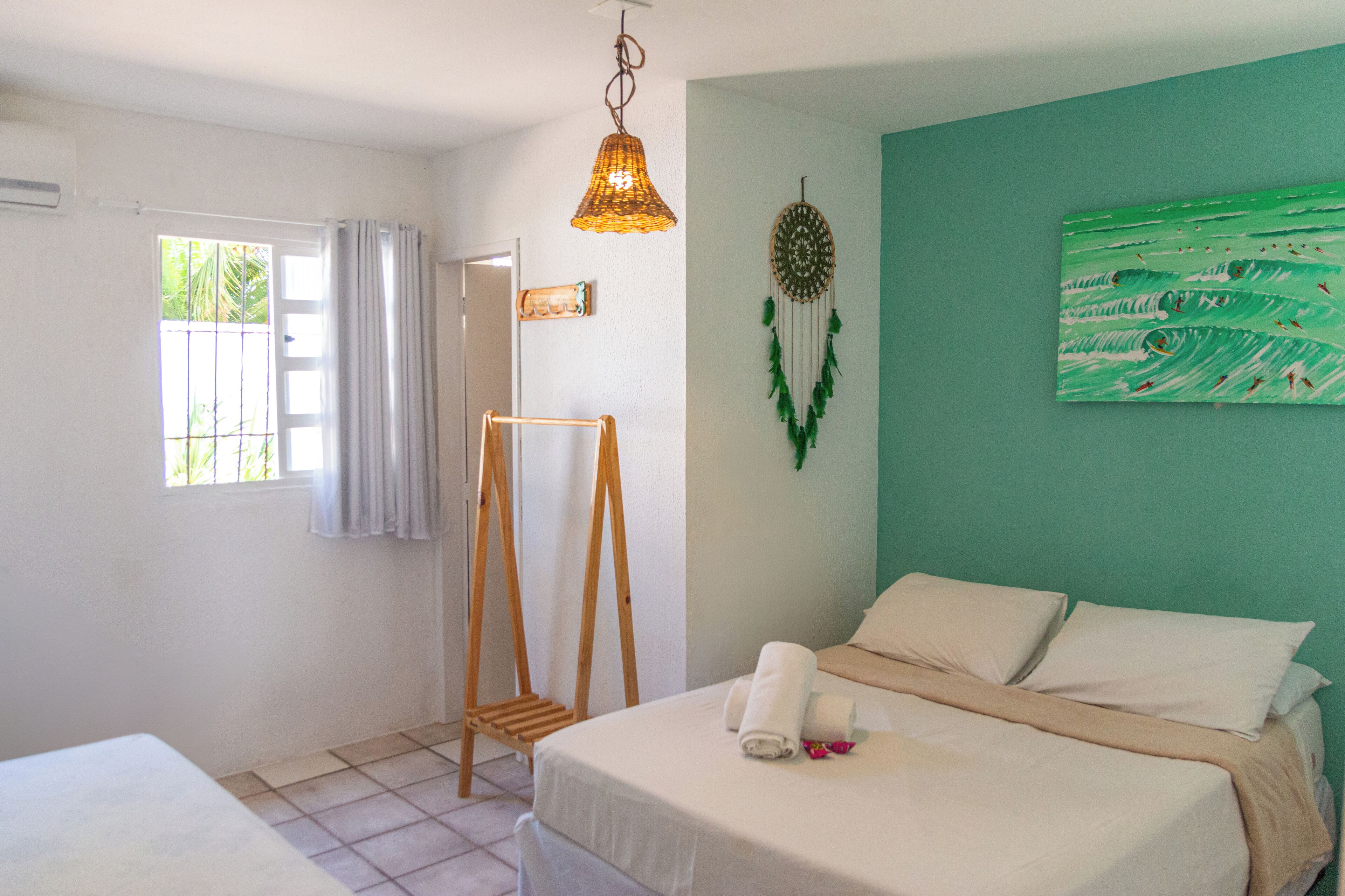 A bedroom with a bed, a wooden ladder, a hanging light fixture, a dreamcatcher, and a painting on the wall.