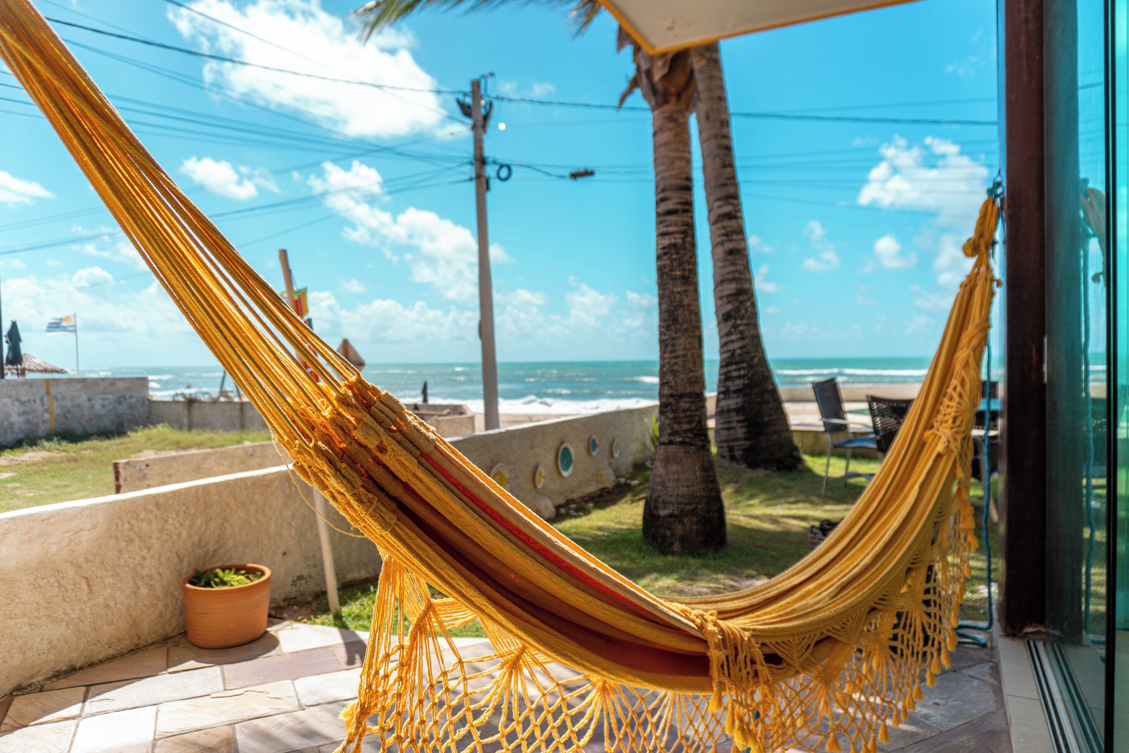A hammock on a patio with a view of the ocean and palm trees.