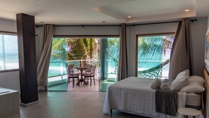 A hotel room with a bed, a small table, and a chair. There is a balcony with a view of palm trees and the ocean. - Pousada La Bella Luna (Ipojuca)