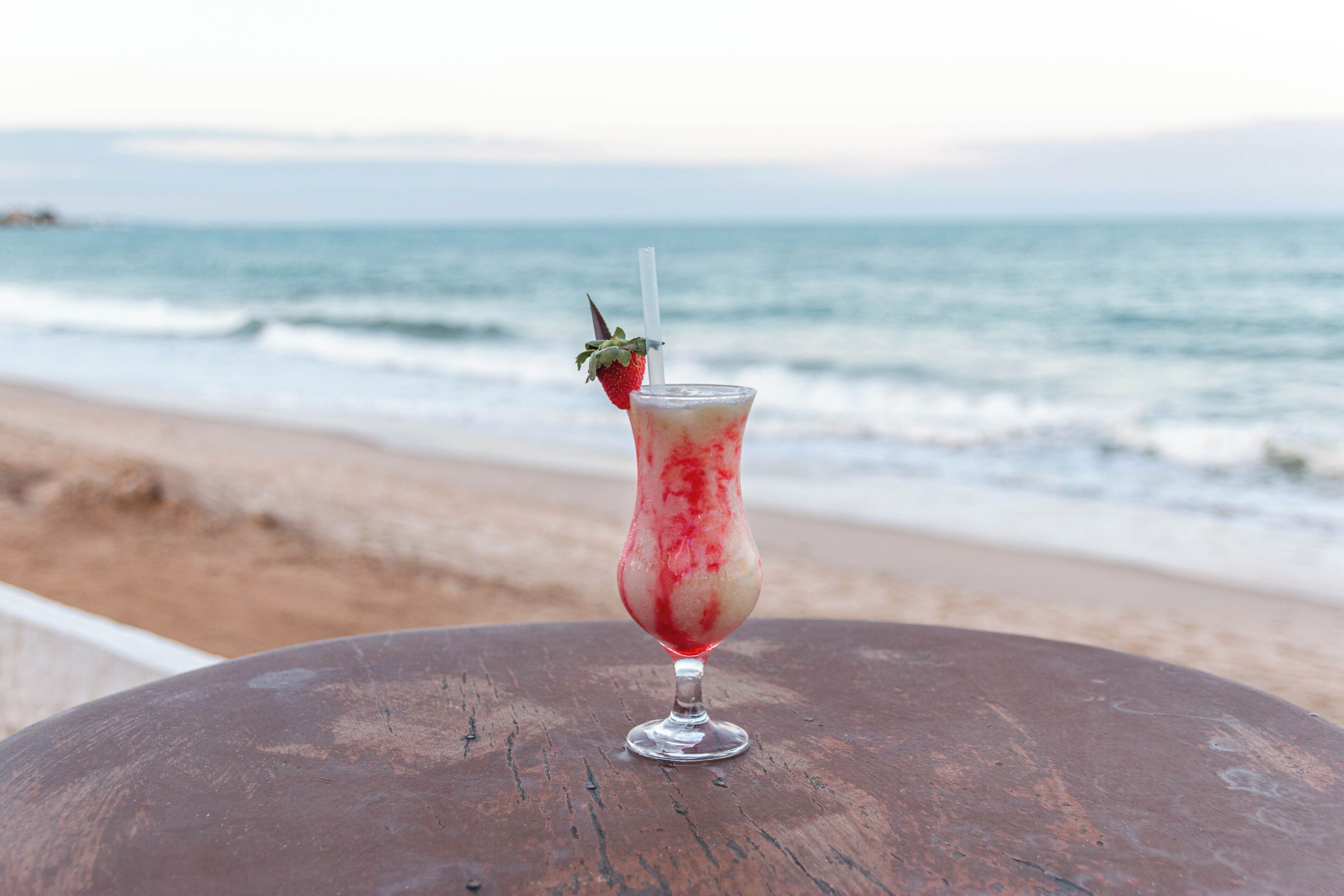 A drink on a wooden table with a view of the ocean.