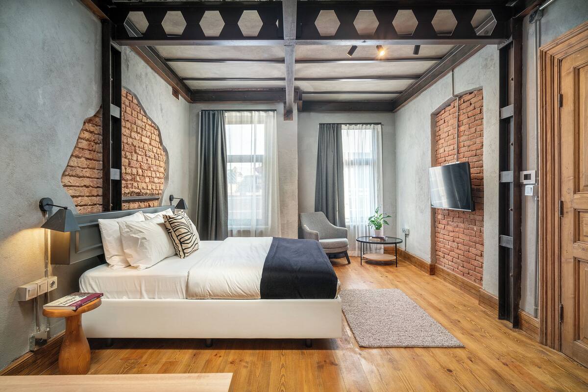 A modern bedroom with a bed, a chair, a TV, and a brick wall.
