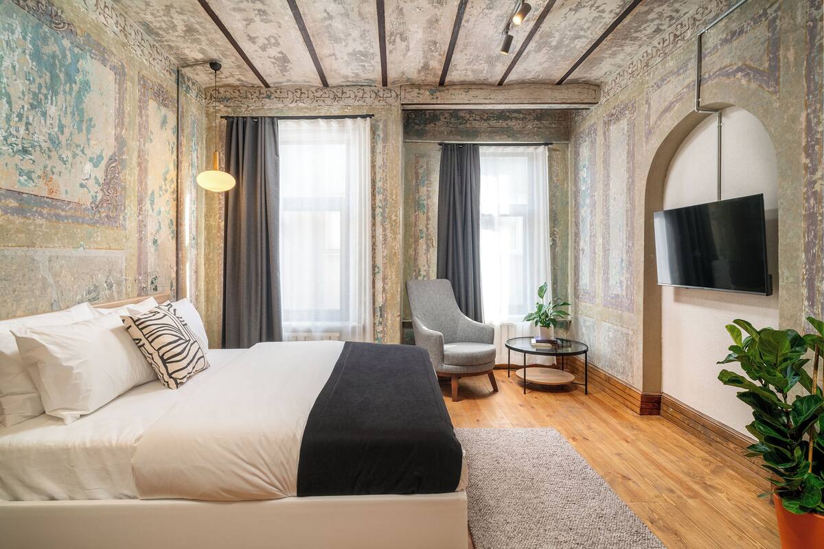 A bedroom with a large bed, a chair, a small table, and a TV.
