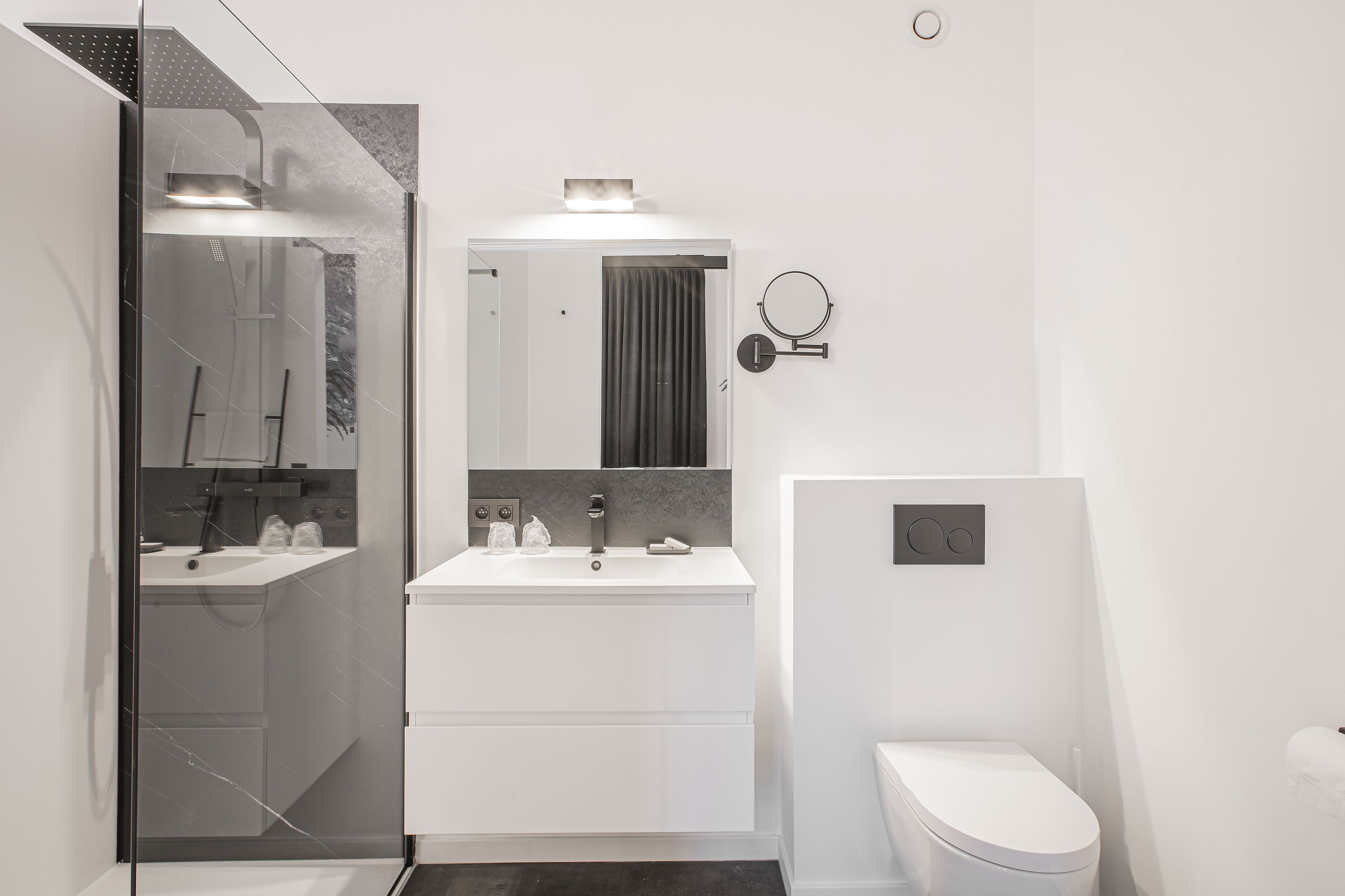 Een moderne badkamer met een glazen douchecabine, een wit wastafelmeubel met spiegel en een toilet.
