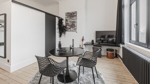 A modern living room with a round table, two chairs, a large window, and a television. - Ribas Guestrooms (Bruges)