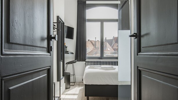 A bedroom with a bed, a radiator, a TV, and a window with curtains. - Ribas Guestrooms (Bruges)