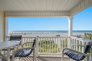 A covered balcony with a view of the beach, featuring two chairs and a table.