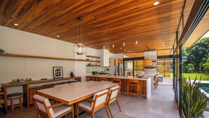 Une cuisine moderne avec des meubles en bois, un grand îlot central et un coin repas comprenant une longue table et des chaises.
