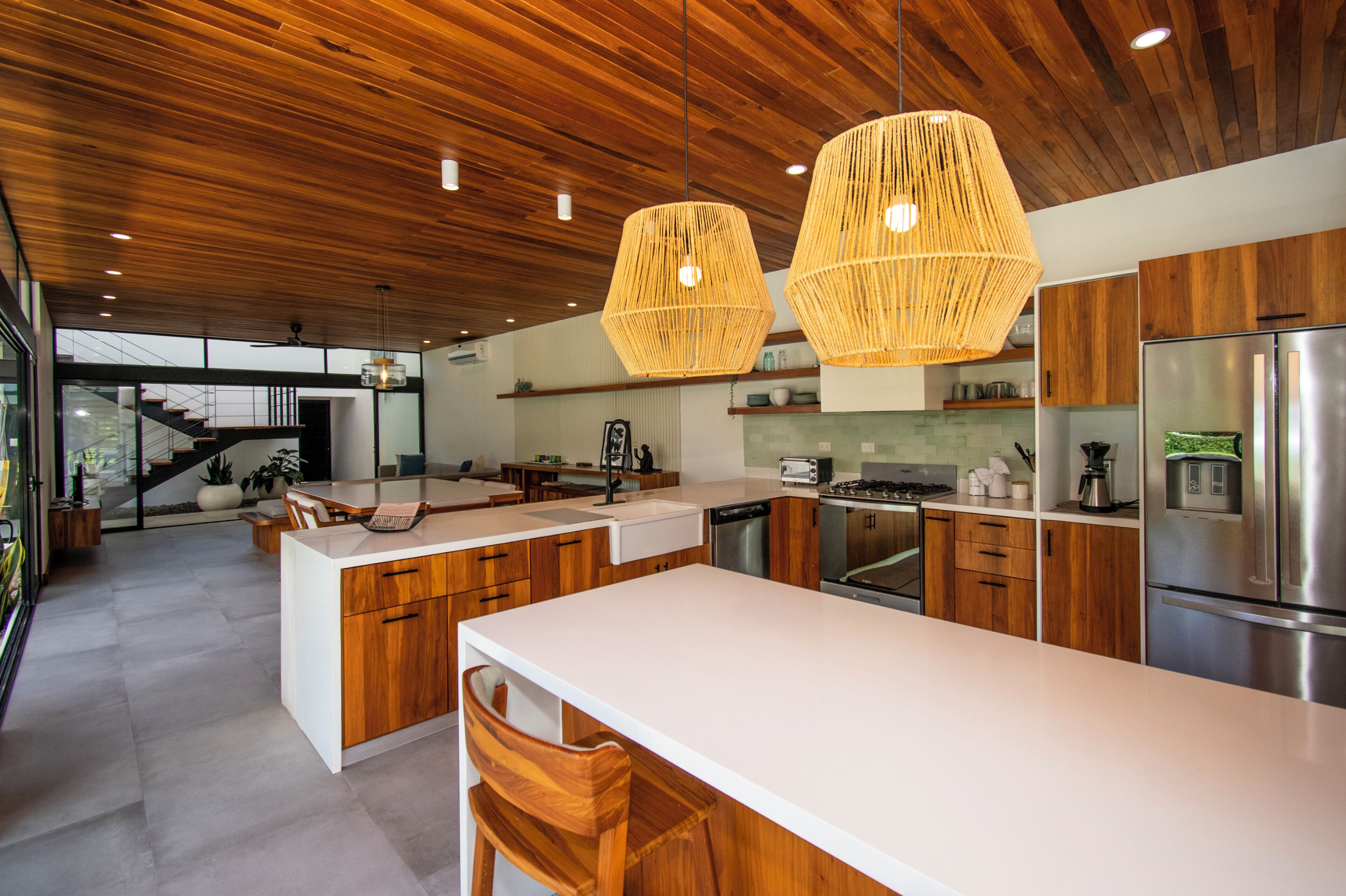 Una cocina moderna con armarios de madera, una isla central, electrodomésticos de acero inoxidable y una escalera que conduce a un nivel superior.