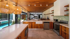 Une cuisine moderne avec des meubles en bois, un îlot central, une cuisinière intégrée et une grande fenêtre donnant sur une piscine.