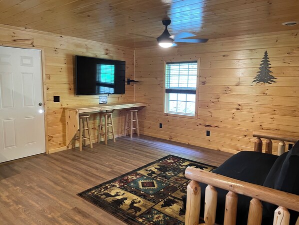 A wooden interior with a bar area, a ceiling fan, a TV, and a patterned rug. - Secluded Cabin with a mountain view, hot tub, full kitchen, and living room. (Putney)