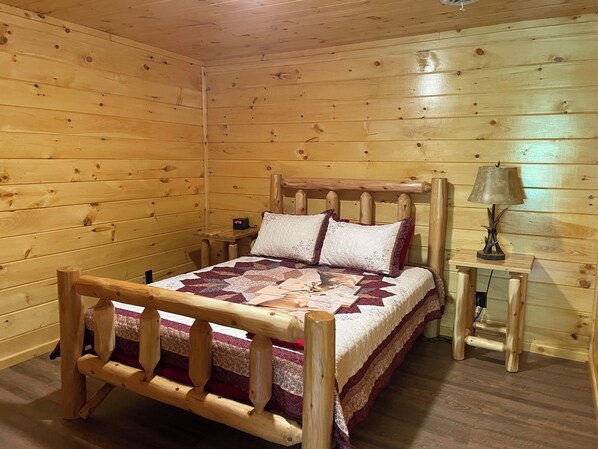A wooden cabin room with a bed, a nightstand, a lamp, and a clock.