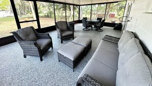 Un'area patio coperta con mobili in vimini, un divano grigio e un tavolo con sedie.