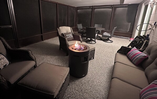 A cozy indoor seating area with a fire pit, cushioned chairs, and a sofa.