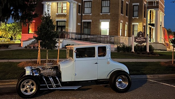 Un'auto d'epoca parcheggiata di fronte a un edificio con una torre dell'orologio illuminata di verde.