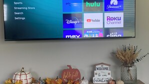 Una TV a schermo piatto montata a parete mostra l'interfaccia di un servizio di streaming con diverse icone di app.