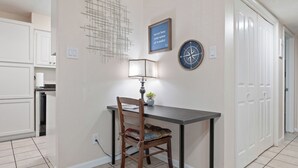 Spiseområde med bord, stol, lampe, billeder på væggen og et køkken i baggrunden.