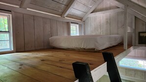 A room with a wooden floor, a bed, and a sloped ceiling with exposed beams.