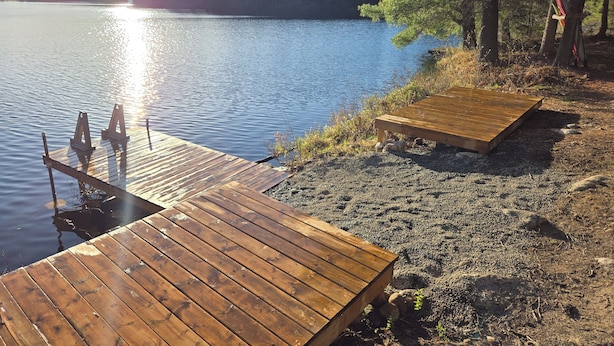 A wooden dock extending into a calm lake, surrounded by trees and a clear sky.