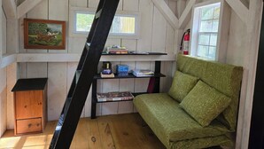 A room with a green sofa, wooden shelves with books, a small wooden cabinet, and a window with a fire extinguisher.