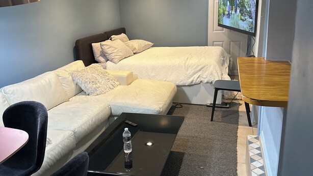 Ein modernes Wohnzimmer mit einer Couch, einem Couchtisch mit einer Wasserflasche, einem Fernseher an der Wand und einem kleinen Holztisch.