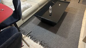 Ein Wohnzimmer mit einem weißen Sofa, einem roten Tisch, einem schwarzen Couchtisch mit einer Wasserflasche und einem grauen Teppich.