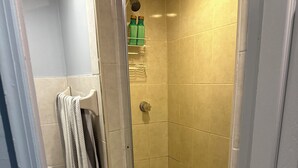 Ein kleiner, abgeschlossener Duschbereich mit gefliestem Boden und Wänden, ein Handtuch auf einem Halter und einer an der Wand montierten Duschbrause.