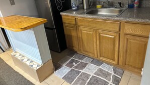 Eine kompakte Küche mit Holzschränken, einer Edelstahl-Spüle, einem Kühlschrank und einer Mikrowelle.