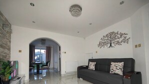 A modern living room with a dark grey sofa, a white radiator, and a dining area with a table and chairs. - Tyburn House, Birmingham B24 with FREE Parking and FREE WiFi (West Midlands)