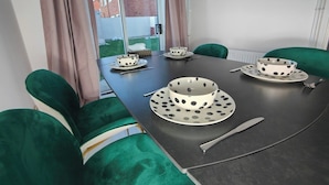 A dining table with four white bowls with black polka dots, two forks, and a knife. The table is surrounded by green upholstered chairs. - Tyburn House, Birmingham B24 with FREE Parking and FREE WiFi (West Midlands)