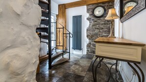 A staircase with a wooden railing, a stone wall with two clocks, a lamp, and a wooden cabinet. - The Coach House - 3 Bedroom - Penally - Tenby (Tenby)