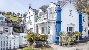 A white building with blue accents, a white picket fence, and various potted plants. - The Coach House - 3 Bedroom - Penally - Tenby (Tenby)