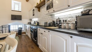 A kitchen with white cabinets, a wooden ceiling, and a dining area with white chairs. - The Coach House - 3 Bedroom - Penally - Tenby (Tenby)