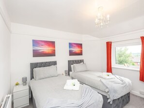 Two single beds with grey headboards and white duvets, a large window, and framed artwork adorn this stylish bedroom.