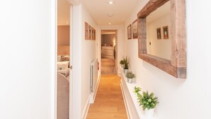 A hallway with a wooden-framed mirror, potted plants, and framed pictures on the walls.
