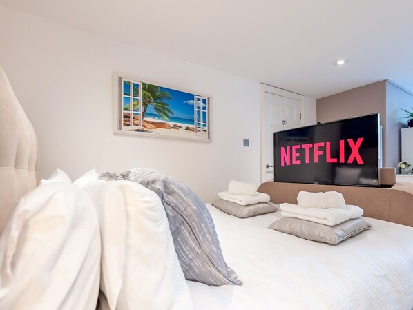 Moderni hotellihuone, jossa on suuri sänky, taulutelevisio ja seinällä ranta-aiheinen taulu.