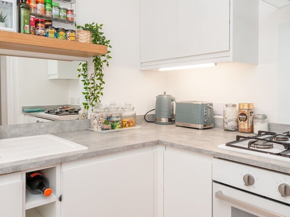 A modern kitchen with white cabinets, a gas stove, a kettle, and various jars on the counter.