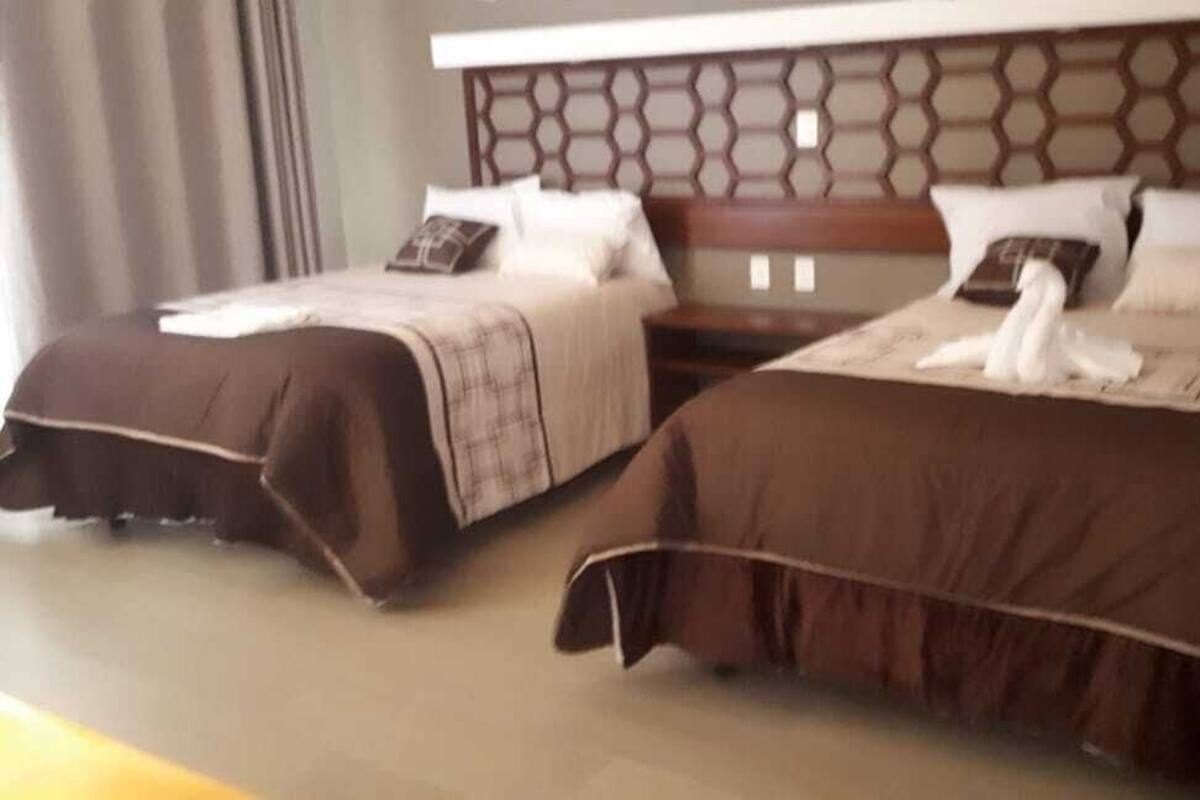 Habitación de hotel con dos camas, cada una con cubrecama marrón y almohadas blancas.