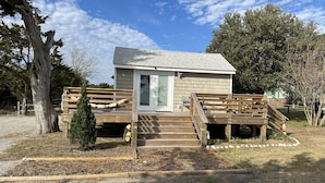 Une petite cabane en bois avec une porte d’entrée, une véranda et un escalier menant à une terrasse.