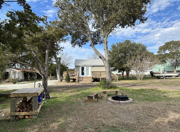 A rustic cabin with a wooden deck, a small fire pit, and a boat docked nearby. - Charming Historic Cottage with Private Waterfront on Core Sound -Pet Friendly (Atlantic)