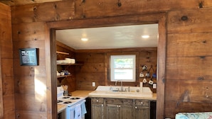 L’intérieur d’une cabane en bois comprend une cuisine équipée d’un poêle, d’un évier et de meubles de rangement en bois.